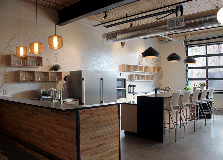 behind the bar of the coffee shop, white leaf-shaped tiles line the walls, glasses, and plants sit in wooden shadow boxes